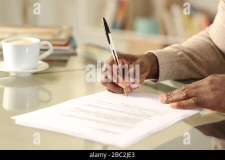 Nahaufnahme eines schwarzen Mannes Hände Gesangsvertrag auf einem Schreibtisch zu Hause Stockfoto