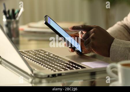 Nahaufnahme der schwarzen Hände mit dem Smartphone mit Laptop auf einem Schreibtisch zu Hause Stockfoto