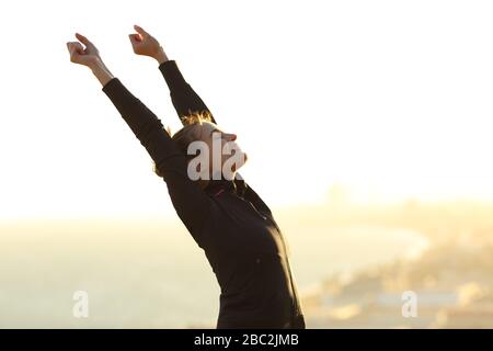 Aufgeregter Läufer, der seine Arme hochhebt und im Freien bei Sonnenuntergang am Stadtrand feiert Stockfoto