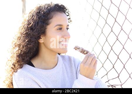 Porträt einer glücklichen jungen Frau, die eine Getreidebar mit Blick auf den Außenbereich isst Stockfoto