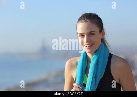 Portrait einer fröhlichen Läuferin, die nach dem Sport mit Küstenhintergrund ein Handtuch am Hals trägt Stockfoto