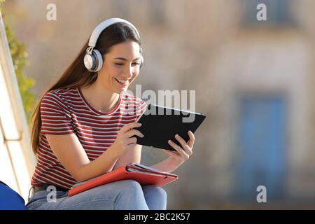 Fröhliche Studenten lernen, Kopfhörer zu tragen und ein Tablet zu verwenden, das im Freien auf einem Universitätsgelände sitzt Stockfoto