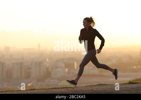 Fröhlicher Jogger, der allein in den Randgebieten der Stadt bei Sonnenuntergang joggt Stockfoto