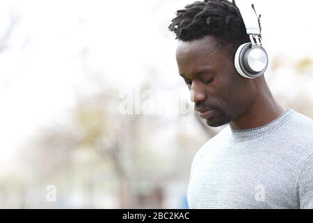 Penibler schwarzer Mann, der Kopfhörer trägt und Musik hört, die im Freien steht Stockfoto