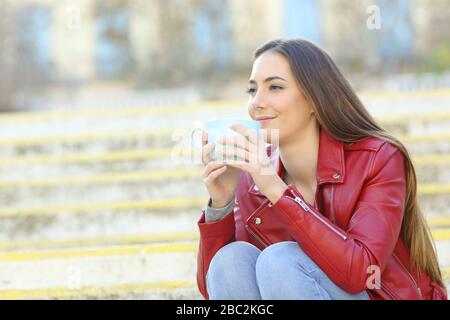 Entspannte Frau mit roter Jacke und einer Tasse Kaffee auf einer Treppe Stockfoto