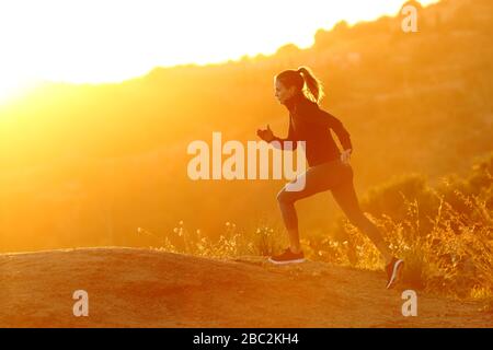 Profil einer Läuferin, die bei Sonnenuntergang in den Bergen läuft Stockfoto