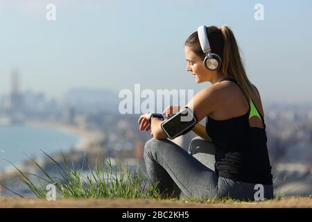 Entspannter Läufer, der Kopfhörer trägt, um Musik auf Smartwatch in den Außenbezirken der Stadt zu hören Stockfoto