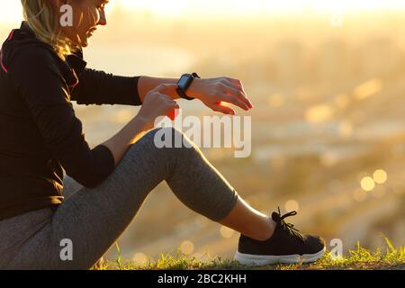 Läufer, die auf dem Boden sitzen und die Smartwatch überprüfen, nachdem sie bei Sonnenuntergang gelaufen sind Stockfoto