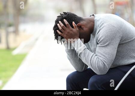 Seitenansicht Porträt eines traurigen, depressiven schwarzen Mannes, der auf einer Bank in einem Park sitzt Stockfoto