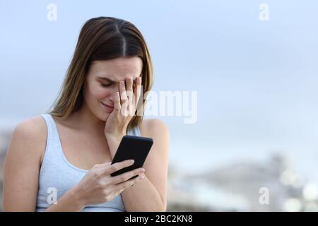 Traurige Frau, die im Freien auf dem Handy schlechte Nachrichten überprüft Stockfoto