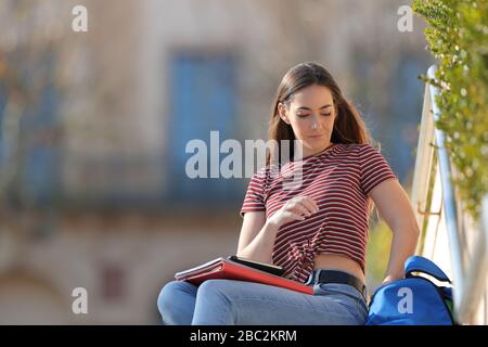 Student nimmt Dinge aus dem Rucksack und sitzt auf einem Campus Stockfoto