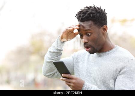 Überraschter schwarzer Mann, der auf dem Handy fantastische Nachrichten in einem Park überprüft Stockfoto