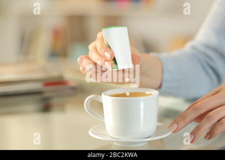 Nahaufnahme von Frau Hand, die zu Hause auf einem Schreibtisch Saccharin-Pillen auf die Kaffeetasse wirft Stockfoto