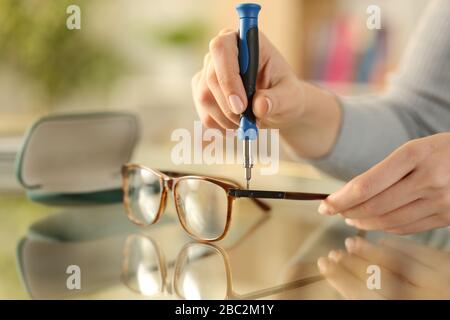 Nahaufnahme der Frau mit der Feststellschraube an der Brille mit einem Schraubendreher auf einem Schreibtisch zu Hause Stockfoto