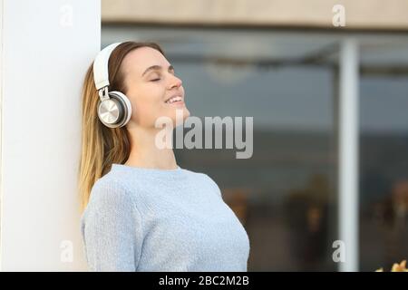 Entspannte junge Frau mit Kopfhörern, die frische Luft auf einer Hotelterrasse atmen Stockfoto