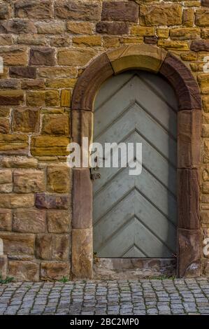 Historische Stadtmauer aus Sandstein mit Holztür und Türrahmen mit Rundbogen aus Sandstein, der mit einem speziellen Schloss eingemeißelt ist Stockfoto