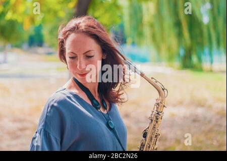 Nahes Porträt einer jungen rothaarigen Frau in einem grünen Park mit Saxofon im Sommer Stockfoto