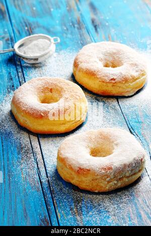 Hausgemachte Donuts mit Puderzucker auf blauem Holzgrund bestreut Stockfoto