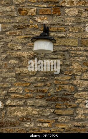 Alte, gepflegte Stadtmauer aus Naturstein mit sehr flachen und breiten Steinen von gelblichem Licht bis hin zu Rostbraun mit einem schönen Vintage-Glas-Exteri Stockfoto