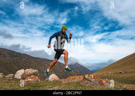 Bärtiger Mannsportler, der im Freien in den Bergen joggt. Training hoch in den Bergen. Sky läuft Stockfoto