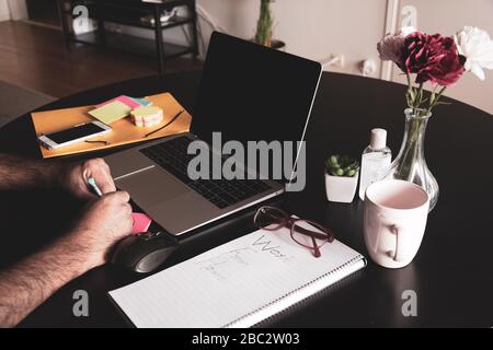 Arbeiten von zu Hause aus mit männlicher Hand in einer klebrigen Notiz mit Laptop, Kaffeetasse, Maus und Notizblock auf einem Esstisch, schweden Stockfoto