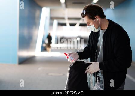 Ein Mann gehört zu einer Coronavirus-Infektion, hat eine Mundmaske, Gummihandschuhe und hat ein Desinfektionsmittel in der Hand Stockfoto