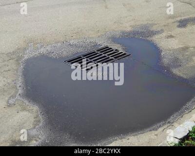 Ablassen einer Tankstelle mit Wasserstagnation mit Spuren von Benzin auf dem Asphalt. Konzept der Kontamination mit Kraftstoffen und Schmiermitteln. Stockfoto
