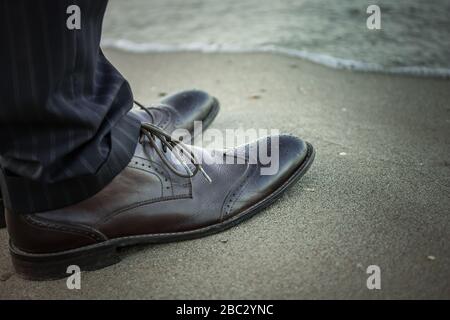 Die Füße eines Mannes in schwarzen Hosen und Schuhen stehen in der Nähe der Küste. Stockfoto