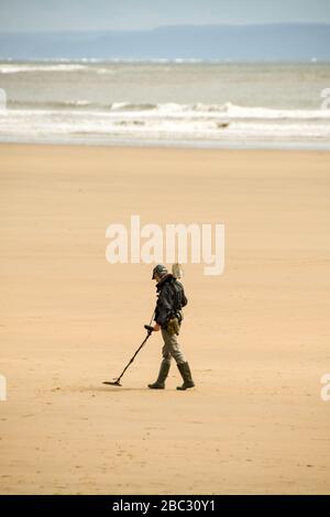 PORTHCAWL, WALES - JUNI 2018: Person mit einem Metalldetektor, der bei Ebbe den menschenleeren Sand des Coney Beach, Porthcawl, durchsucht Stockfoto