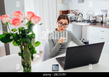 Arbeiten Sie von zu Hause aus während der Quarantäne des Coronavirus. Frau arbeitet auf Laptop in der Küche. Freiberufler spricht mit Kollegen online Stockfoto