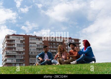 Zwei junge hispanische Männer genießen Musik mit einer Gitarre neben zwei kaukasischen Mädchen in einem Stadtpark, Bild enthält Platz für Text Stockfoto