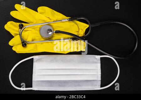 Hygienemaske für Schutz, Handschuhe und Stethoskop. Zubehör für Ärzte und Patienten zum persönlichen Schutz. Dunkler Hintergrund. Stockfoto