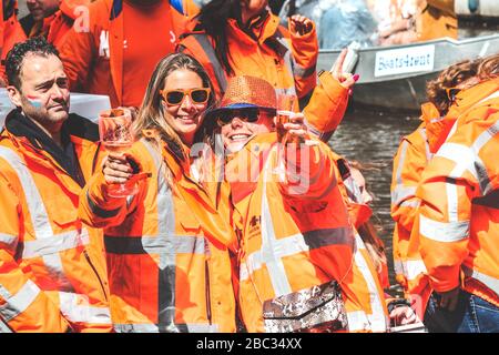 Amsterdam, Niederlande - 27. April 2019: Frauen auf dem Partyboot in nationaler orangefarbener Farbe feiern den Kings Day, Koningsdag, den Geburtstag des niederländischen Königs Willem-Alexander. Brille anheben. Stockfoto