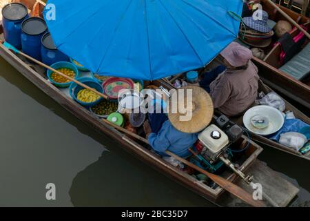 Boot, das Produkte auf dem Amphawa Floating Market, Thailand mit Schirm und Frauen in traditionellen Hüten verkauft Stockfoto