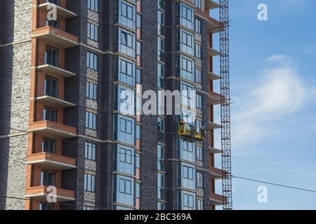 Bauradträger an der Hintergrundfassade des im Bau befindlichen Gebäudes. Fassadenarbeiten mit Bauwiege Stockfoto