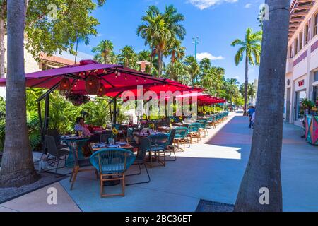 Wunderschöner Blick auf die Landschaft des Cafés im Freien. Blaue Stühle unter roten Sonnenschirmen auf grünen Bäumen und blauem Himmel. Miami. USA. Stockfoto