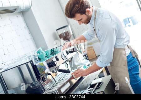 Kaffeelaffee. Junger Barista im Café Reinigung Espressomaschine nachdenklich Stockfoto