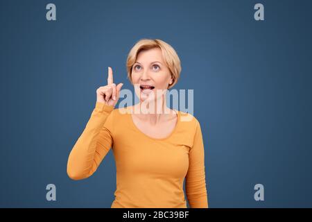 Freistil. Reife Frau stehend isoliert auf blau zeigt auf Kopie Raum inspiriert von kreativen Idee Stockfoto