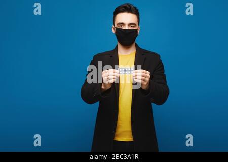 Junger gutaussehender Mann in einer schützenden medizinischen Maske, die Pillen in den Händen hält. Virenschutz und Gesundheitskonzept Stockfoto