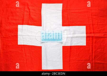 Coronavirus in der Schweiz. Schützende chirurgische Gesichtsmaske auf Schweizer Nationalflaggen. Schweizer Quarantäne, Schutzkoronavirus Symbol des Arztes, der Krankenschwester Stockfoto