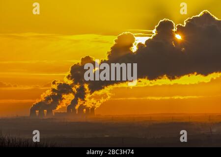 Fernblick von den Yorkshire Wolds, Großbritannien von den Kühltürmen einer Power Station in der Nähe von Drax in North Yorkshire, mit der Sonne, die hinter dem Vapor Trail liegt Stockfoto