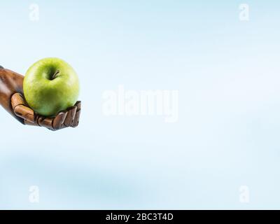 Frischer grüner apfel in der Palme aus Holzhand auf Blau Stockfoto