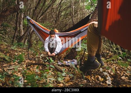 Ein Mann, der in einer Hängematte im Wald sitzt, bereitet sich auf das Wandern vor Stockfoto
