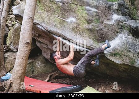 Ein männlicher Bergsteiger klettert draußen auf einen Felsen Stockfoto