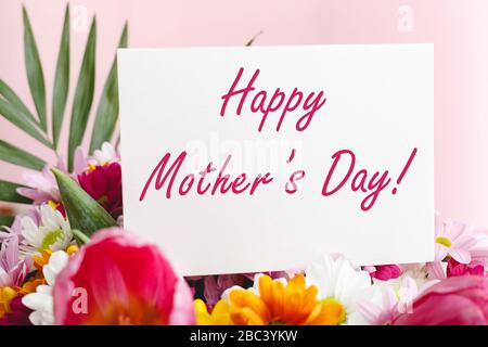 Happy Mothers Day Text auf Geschenkkarte in Blumenstrauß auf pinkfarbenem Hintergrund. Grußkarte für Mama. Blumenlieferung, Glückwunschkarte in Blumen für Stockfoto