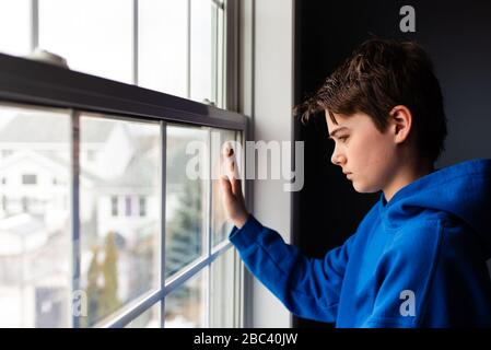 Zwischen Jungen, der aus einem Fenster in einem dunklen Raum schaut. Stockfoto