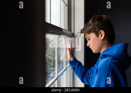 Zwischen Jungen, der aus einem Fenster in einem dunklen Raum schaut. Stockfoto