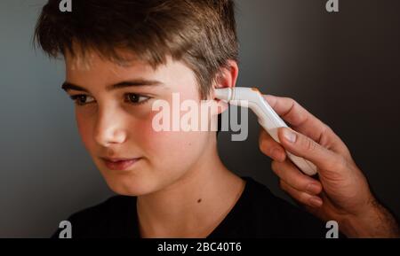 Zwischen Jungen bekommen Temperatur mit einem Ohrthermometer genommen. Stockfoto