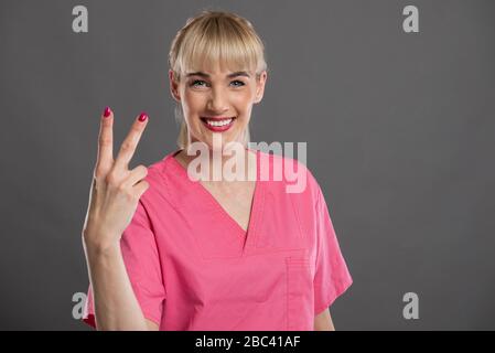 Porträt der jungen attraktiven weiblichen Krankenschwester mit der Nummer zwei auf grauem Hintergrund und Werbefläche für Kopien Stockfoto