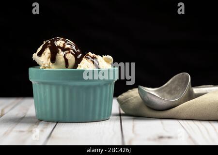 Schaufeln Vanilleeis in einer Schüssel, die mit Schokoladensirup verraucht ist. Stockfoto